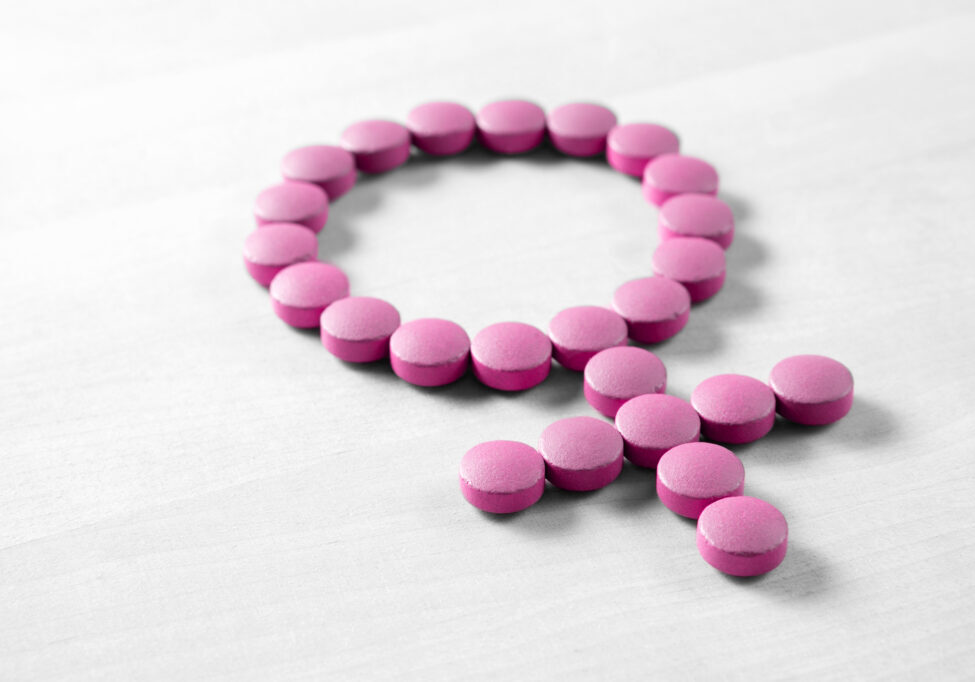 Female health. Gender symbol made from pink red pills or tablets on wooden table
